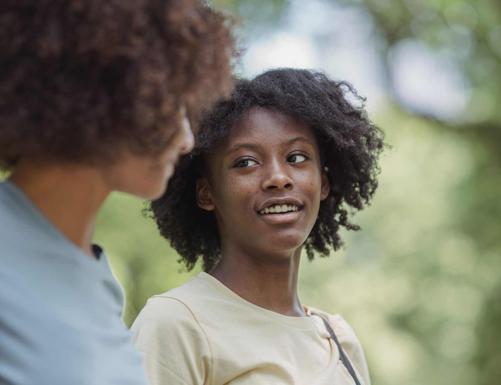 Two young women chatting happily while walking in a lush green park.